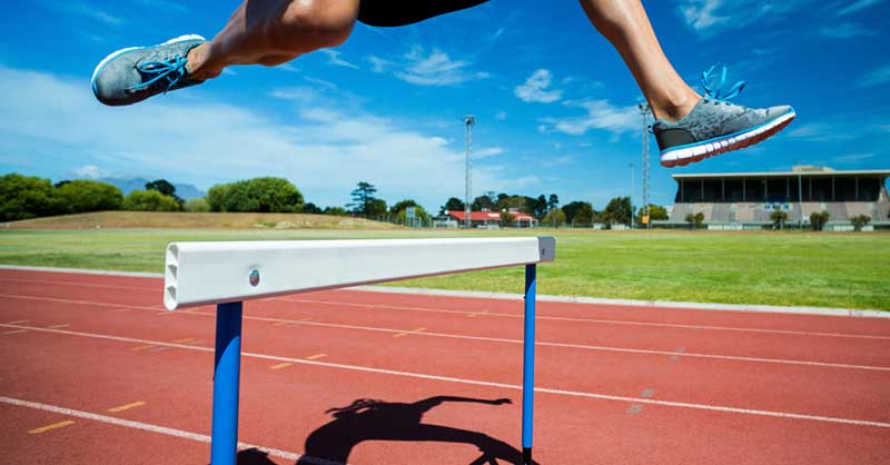 track and field runner jumping over a hurdle